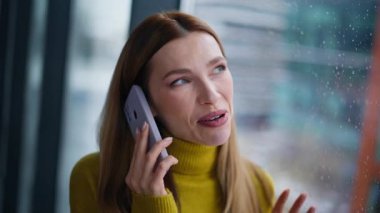 Kapalı çekim neşeli sarışın yağmurlu pencerenin yanında cep telefonunu arıyor. Akıllı telefondan konuşan, gülümseyen bir kadın şehir manzaralı haberleri paylaşıyor. Hoş bir bayan cep telefonuyla sohbet ediyor. Evde dinleniyor..