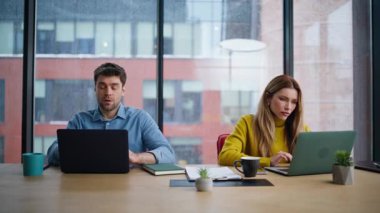 Şirket çalışma alanına dizüstü bilgisayar arayan motivasyonsuz iş arkadaşları. Yorgun erkek kadın ofis panoramik penceresinin yanında aşırı yüklü iş projesi. İki yönetici birlikte çalışırken yorulduklarını hissediyorlar..