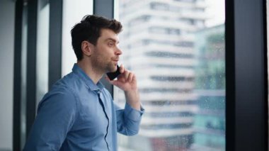 Ciddi bir yönetici cep telefonunu arıyor. Ofis penceresinden yağmur damlalarını kapatıyor. Akıllı telefondan projeyi tartışan yakışıklı profesyonel bir çalışan. Genç işadamı cep telefonundan konuşuyor. Şehir manzarasının keyfini çıkarın.