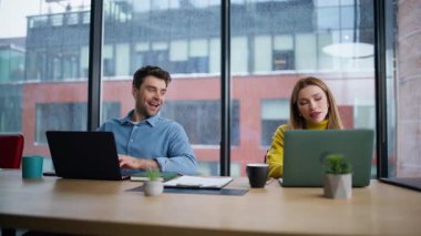 İş yerinde gülümseyen meslektaşlar yakın plan konuşuyor. Dost canlısı bir yönetici kadın dizüstü bilgisayarına bakıyor ve açık alanda harika bir iş çıkardığını tartışıyor. Çalışma alanında işbirliği yapan mutlu iş arkadaşları iş başarısını paylaşıyor