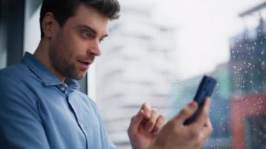 Heyecanlı yönetici yağmurlu pencere önünde akıllı telefon mesajını sevinçle karşılıyor. Finansal gelir bildirimi alan aşırı mutlu iş adamı. Duygusal kazanan cep telefonuyla mutlu görünüyor..