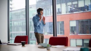 İş adamı, panoramik pencerenin yanında bekleyen bir cep telefonundan şikayetçi. Stresli yöneticilerin akıllı telefon konuşmalarında tartışması duygusal olarak işaret ediyor. Endişeli adam cep telefonu konuşmasından memnun değil.