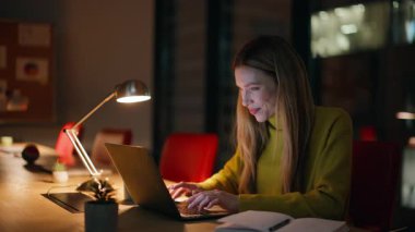 Gece iş yerinde bilgisayarı bilgisayara yüklemek. Karanlık ofiste ışık altında çalışan gülümseyen bir iş kadını. Gece geç saatlerde online proje geliştiren serbest yazardan esinlendim. Fazla mesai kavramı