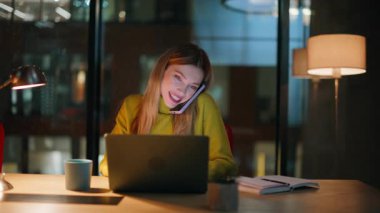 Gülümseyen bayan gece ofisinden arıyor. Laptop ekranını kapatıyor. Kadın yönetici karanlık iş yerinde cep telefonuyla iş görüşmeleri yapıyor. Fazla mesai yapan hevesli iş kadını..