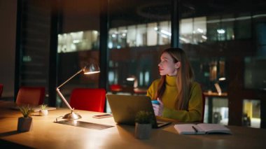 Gece işçisi lamba ışığı altında kahve içiyordu. Sakin bir iş kadını laptopta çalışırken içeceğini yudumluyor. Güzel bir kadın gece geç saatlerde iş yerinde bilgisayar başında mola veriyor..