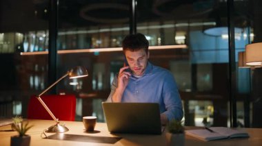 Şirketin profesyonel konuşan cep telefonu gece ofisinde yakın plan çekimde. Gülümseyen yönetici, karanlık işyerinde oturarak akıllı telefon görüşmesine danışmanlık yapıyor. Akıllı serbest çalışan cep telefonuyla fazla mesai yapıyor..