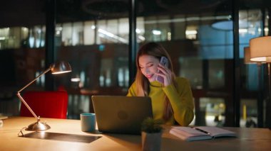 İş kadını, karanlık ofiste cep telefonuyla konuşuyor. Gülümseyen bir kadın cep telefonunu arıyor. Mesai saatleriyle meşgul. Pozitif kadın girişimci gece işyerinde akıllı telefon ile işi tartışıyor.