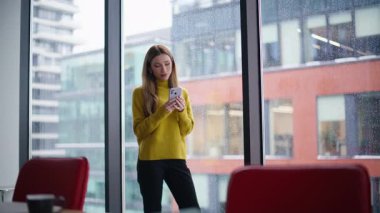 İş yerindeki cep telefonunda sosyal medyayı karıştıran rahat bir bayan. Sakin bir iş kadını panoramik pencere manzaralı akıllı telefon mesajı okuyor. Cep telefonunu izleyen çekici bir kadın..