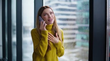 Neşeli sarışın, yakın arkadaşlarıyla akıllı telefon paylaşımı hakkında konuşuyor. Gülümseyen güzel bir kadın panoramik pencerenin önünde cep telefonuyla konuşuyor. Mutlu iş kadını, keyifli telefon konuşmalarının keyfini çıkar..