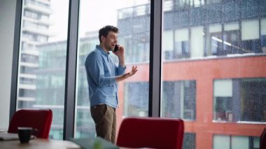 Ofiste gülümseyen profesyonel bir şirket cep telefonunu arıyor. Mutlu iş adamı, panoramik pencerenin yanında duran akıllı telefonla başarılı bir pazarlığın tadını çıkarıyor. Neşeli yönetici cep telefonu konuşmasını bitirdi.