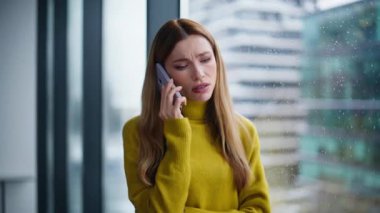 Sorunlu kadın yönetici ofis penceresinden cep telefonunu arıyor. Endişeli iş kadını cep telefonu konuşmasında kötü haberler duyuyor. Kadın girişimci endişeli akıllı telefon konuşmaları stresli.