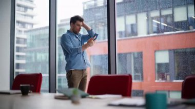 Ofiste umutsuzluk hisseden girişimci cep telefonu bankacılığı uygulamasına göz atıyor. Kafası karışmış işadamı akıllı telefon mesajı okuyor panoramik pencerenin yanında duruyor. Hüsrana uğramış adam mali krizden endişeli..