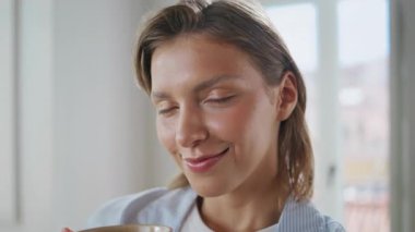 Elinde parlak oda portresiyle kahveyi tutan gülümseyen kadın. Tatmin olmuş bir kadın kameraya bakıyor ve evde sakin bir sabah geçiriyor. Neşeli kısa saç modeli. İç mekanda elinde içecek bardağıyla poz veriyor..