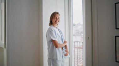 Dairenin penceresinde gülümseyen kadın kendini mutlu hissediyordu. Pijamalı sıradan bir sabah kızı. Kameraya bakıyor. Huzurlu ev atmosferinin tadını çıkarıyor. İçeride mutlu, rahat bir kadın. Yaşam tarzı rutin kavramı