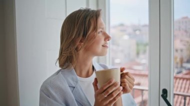 Parlak bir dairede elinde bardak tutan portre kızı kendini yalnız hissediyor. Gülümseyen bayan, sakin bir sabahın tadını çıkarıyor. Şehir manzarasında poz veriyor. Evde sıcak bir içecekle rahatlamış kadın rüyası