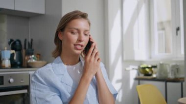 Ev hanımı cep telefonuyla konuşuyor. Genç bir kadın modern mutfakta oturmaktan zevk alıyor. Pijamalı, cep telefonuyla konuşan neşeli, arkadaş canlısı kız. İçerde iyi haberleri paylaşan bir kadın.. 