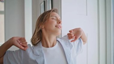 Sabah apartmanında kollarını açan mutlu bir kız. Aydınlık odada dinlenen dingin bir kadın kendini yenilenmiş hissediyor. Gülümseyen kısa saçlı bayan modern evde dinleniyor. Yaşam tarzı rutin kavramı.