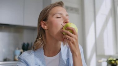 Modern bir dairede elma yiyen yakın plan kadın. Gülümseyen kız sabah yediği yeşil meyvenin tadını çıkarıyor. Neşeli kadın taze organik yemeğin tadını çıkarıyor. Sağlıklı besin konsepti.