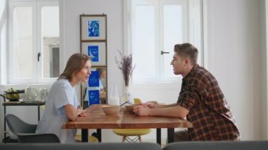 Sakin bir sabahta mutfak masasıyla iletişim kuran rahat ortaklar. Gülümseyen çift kahvaltısı modern iç mekanda konuşuyor. Genç bir kadın hafta sonu yemeğinden zevk alıyor. Mutlu eşler yaşam tarzı kavramı.