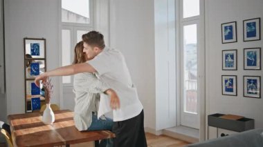 Yeni evde aile taşınma gününü kutluyor. Mutlu kız, parlak dairede anahtar kucaklayan adamı fırlatıyor. Neşeli yeni evliler heyecanla kucaklaşıyorlar. Sevgi dolu çift birlikte yaşamaktan zevk alıyor.