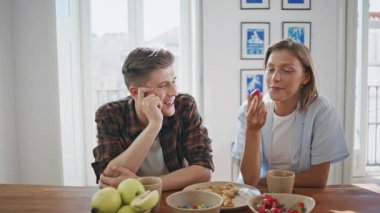 Sıcak mutfakta kadın kahvaltını seven bir adam. Genç ve mutlu bir aile hafta sonu sakin bir sabahta sıcak kahvenin tadını çıkarıyor. Pijamalı kaygısız partnerler evde yemek yiyor. Romantik ilişki kavramı.