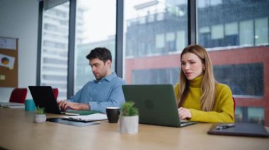 Ofis panoramik penceresinde dizüstü bilgisayarlar yazan odaklanmış yöneticiler. Kadın, tavsiye isteyen akıllı adama bilgisayar ekranı gösteriyor. Arkadaş canlısı iş adamı çalışma alanındaki iş arkadaşına çevrimiçi görevde yardım ediyor