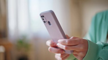 Modern oturma odasında cep telefonuyla mesajlaşan bir kadın. Gülümseyen kadın akıllı telefondan mesaj atıyor rahat evde internet iletişiminin keyfini çıkarıyor. Sosyal medyayı cep telefonundan izleyen mutlu kız öğrenci.