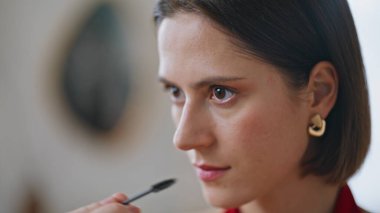 Yansımaya bakarak rimel süren yakın plan kadın. Portre stili bir kadın dairede fırça kullanarak doğal güzelliği vurguluyor. Zarif esmer, sabah güzellik rutininde makyaj yapıyor..