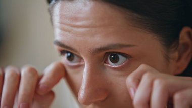 Kapalı alanda parmaklarıyla göz altı derisi masajı yapan yakın plan bir kız. Ev cildine odaklanan güzel bir genç kadın portresi. Sakin esmer, yüz kaldırma ameliyatından hoşlanıyor..