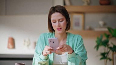 Modern bir apartman dairesinde cep telefonu mesajları yazan bir kadın. Evde akıllı telefon tutan gülümseyen genç bir kadın. Rahat kız cep telefonu uygulamasından online alımlar seçiyor.