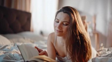 Yatakta kitap okuyan bir kadın, sakin bir ev sabahının tadını çıkarıyor. Rahat esmer, elinde ilginç bir edebiyatla evde yatıyor. Huzurlu bayan rahat yatak odasında dinlenirken romanlara daldı..