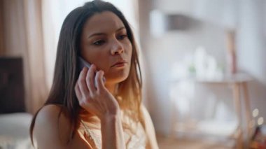 Endişeli esmer, konuşan cep telefonlu daire yatağı, yakın plan. Endişeli kadın, güneşli bir evde uyandıktan sonra cep telefonunu arıyor. Stresli kız sabah erken saatlerde akıllı telefon konuşması yapar..