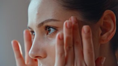 Sabah cilt bakımında cilde dokunan yakın plan kız. Kırışıkların önlenmesi için yüz masajı yapan çekici genç bayan portresi. Ciddi esmer, banyoda doğal bir güzelliğe benziyor..