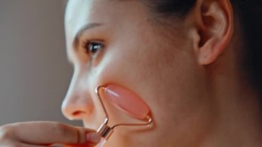 Yüzüne masaj yapan, pürüzsüz, parlak cildine özen gösteren bir kız. Evdeki doğal kuvars aletini kullanarak kendine masaj yapan güzel bir kadın. Rahat esmer, anti-yaş cilt prosedürünün tadını çıkarın..