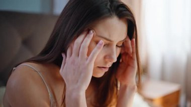 Uyanmış kız apartman yatağında otururken baş ağrısı çekiyor. Stresli bir kadın sabah migreni olan tapınaklara masaj yapıyor. Üzgün esmer, yatak odasında baş ağrısı çekiyor. Sağlık sorunu kavramı