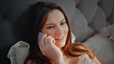 Esmer, yatakta cep telefonuyla konuşuyor. Sabahın erken saatlerinde kapanış. Portre gülümseyen kadın, yatak odasında oturarak akıllı telefon sohbetinin tadını çıkarıyor. Mutlu bayan güneşli ev odasında cep telefonunu arıyor..