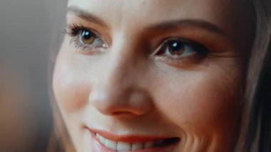 Neşeli bir gülümsemeyle geleceğe bakan lüks bir kadın portresi. Kapalı mekandaki birine gülümseyen parlak makyajlı neşeli esmer. Zarif, koyu renk gözlü kadın modeli kadınlığını ifade ediyor..