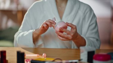 Ev banyosunda kadın eli kozmetik kavanozu açıyor. Gülümseyen esmer, cilt aynasına nemlendirici krem sürüyor. Beyaz cüppeli güzel bayan sabah rutininin tadını çıkarıyor..