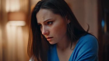 Sorunlu kadın akşam evde oturup sorunlarını yakından düşünüyor. Stresli esmer, başını tutuyor. Karanlık dairede duygusal gerginlik yaşıyor. Endişeli kadın lamba ışığı altında kaygılanıyor..