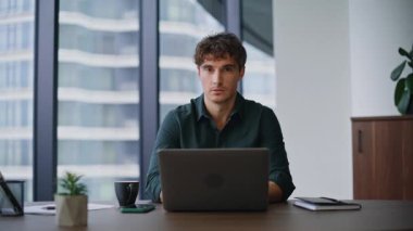 Şirket işyerindeki panoramik pencereli bilgisayarı araştırmada başarılı oldu. Ofiste online çalışan mutlu bir iş adamı. Modern çalışma alanında yakışıklı, uzman gülümseyen kamera..