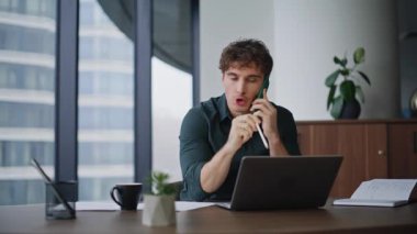 Sinirli iş adamı cep telefonuyla bağırıyor ofis masasında dizüstü bilgisayar gibi oturuyor. Sinirli CEO, cep telefonuyla duygusal jestler yaparak tartışıyor. Öfkeli yönetici iş yerinde stresli akıllı telefon konuşmasını bitirdi.