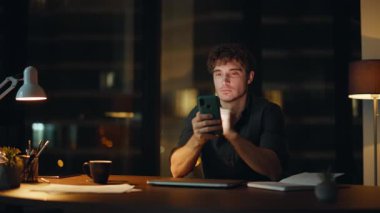 Karanlık Ofis 'te profesyonel akıllı telefon tarayıcısı. Mesajı yakın çekimde okuyor. İş gününün sonunda cep telefonundan sosyal medyayı izleyen gülümseyen iş adamı. Geceleri maaş bildirimi alan serbest çalışan mutlu..