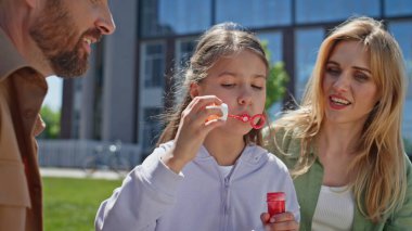 Küçük kız parkta sabun köpüğü üflüyor ve ailesi yakın çekim yapıyor. Neşeli bir aile evinin yanındaki yeşil çimlerde piknik yapıyor. Erkek kadın çift ve kız çocuğu dışarıda eğleniyorlar. Tatil kavramı