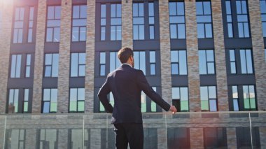 İş adamı güneşli şehir manzarasında modern mimariyi izliyor. Tek başına duran resmi girişimci mesafeyi arıyor. Şık erkek işçi şehir terasında dinleniyor. Profesyonel yaşam tarzı kavramı