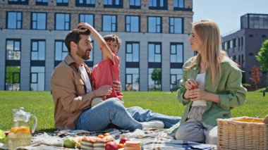 Neşeli ebeveynler parkta çocuk çocukla vakit geçiriyorlar. Mutlu aile birlikte yemek yerken eğleniyor. Küçük çocuk babasıyla battaniyede oynuyor. Kadın ve erkek piknikte konuşuyor, dışarıda lezzetli bir öğle yemeği hazırlıyorlar. 