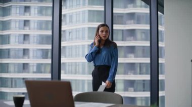 Memnun olmayan kadın CEO 'nun elinde ofis panoramik penceresinin yanındaki belgeleri tutarak akıllı telefonu araması. Sinirli iş kadını cep telefonuyla kontrat hatasından yakınıyor. Sinirli bayan telefonda sorun tartışıyor..