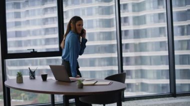 Yönetici, ofis masasına yaslanarak akıllı telefon pazarlığı yapıyor. Lüks iş yerinde panoramik pencereli cep telefonuyla konuşan zarif bir iş kadını. Başarılı kadın patron arıyor..