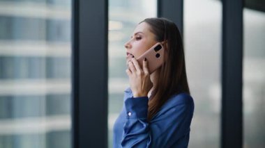 Profesyonel yönetici, ofis penceresine yakından bakarak akıllı telefondan danışmanlık yapıyor. Güzel bir iş kadını şirket binasında cep telefonunu arıyor. Kendine güvenen bayan çalışan konuşuyor..
