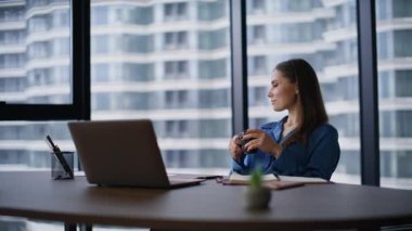 Kendine güveni tam patron, modern ofis koltuğunda oturmuş elinde kahve fincanı tutuyor. Şık bir iş kadını iş yerinde dinleniyor panoramik pencereden şehir manzarası izliyor. Güzel iş kadını dizüstü bilgisayardan mesaj alıyor.