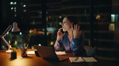 Fazla mesai yöneticisi cep telefonundan konuşuyor. Gece çalışma alanında dizüstü bilgisayar arıyor. Stresli iş kadını akıllı telefondan arıyor karanlık ofiste iş sorununu tartışıyor. Endişeli kadın çalışan hoşnutsuz bir konuşma yaptı..